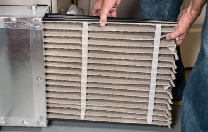 man removing a dirty air filter from a furnace