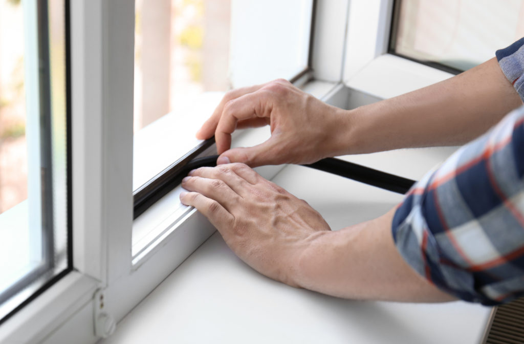 Person adding weather stripping to a window to prevent heat loss and lower heating bills.